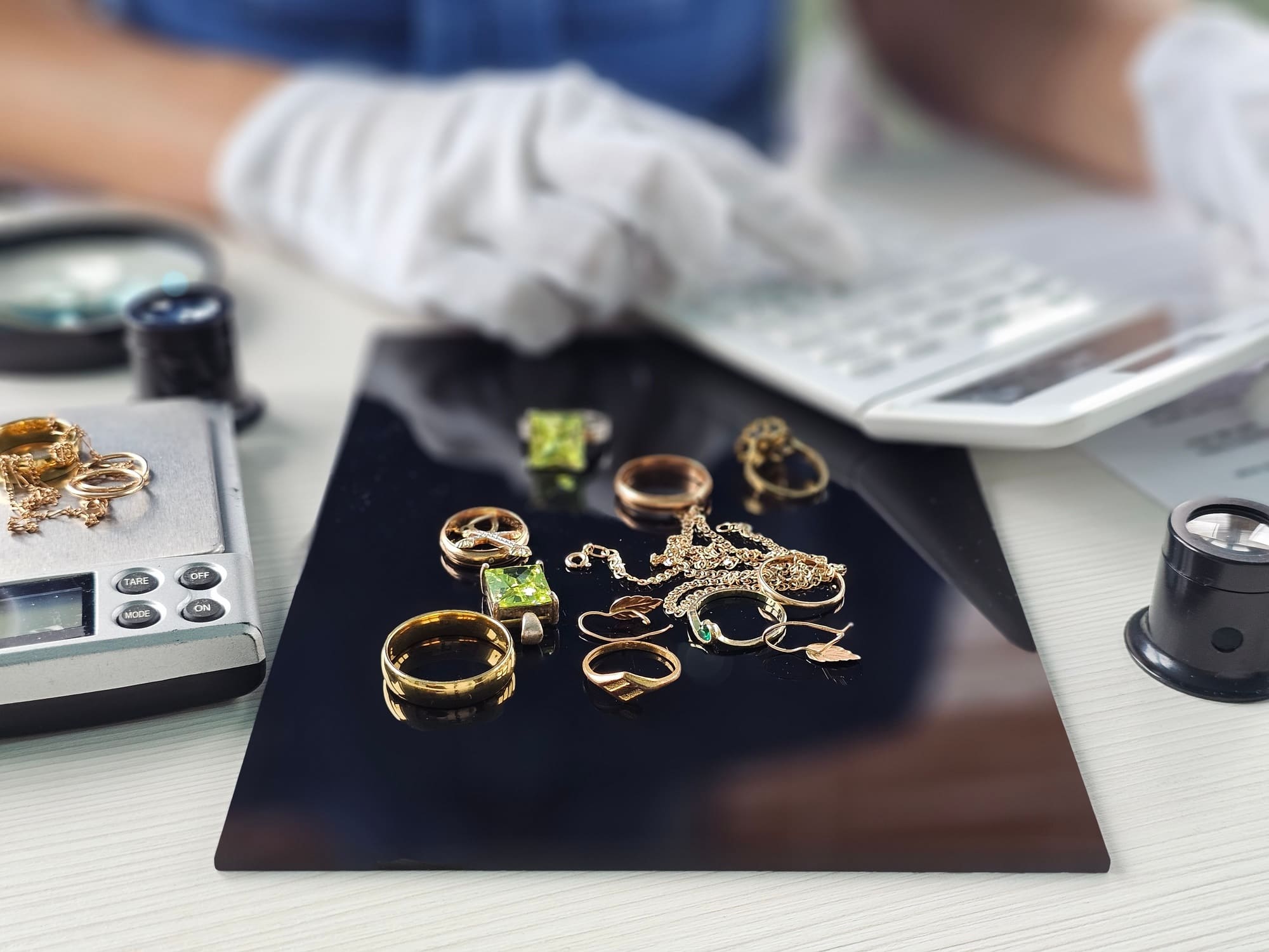 Bijoux en or disposé sur une balance dévaluation, manipulés avec des gants lors d'une estimation pour le rachat d'or en bijouterie.