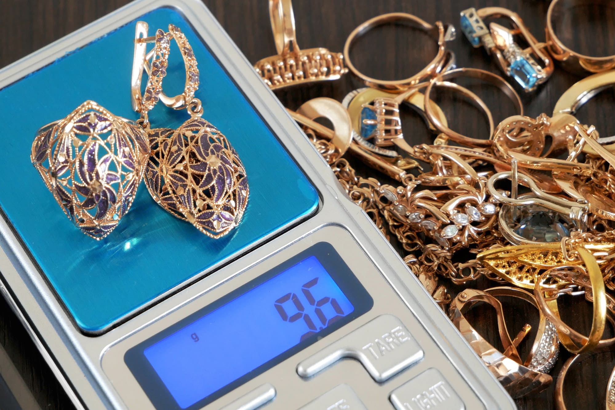 Balance affichant des bijoux en or pesés pour la revente, avec plusieurs bagues, chaîne et boucles d'oreilles.